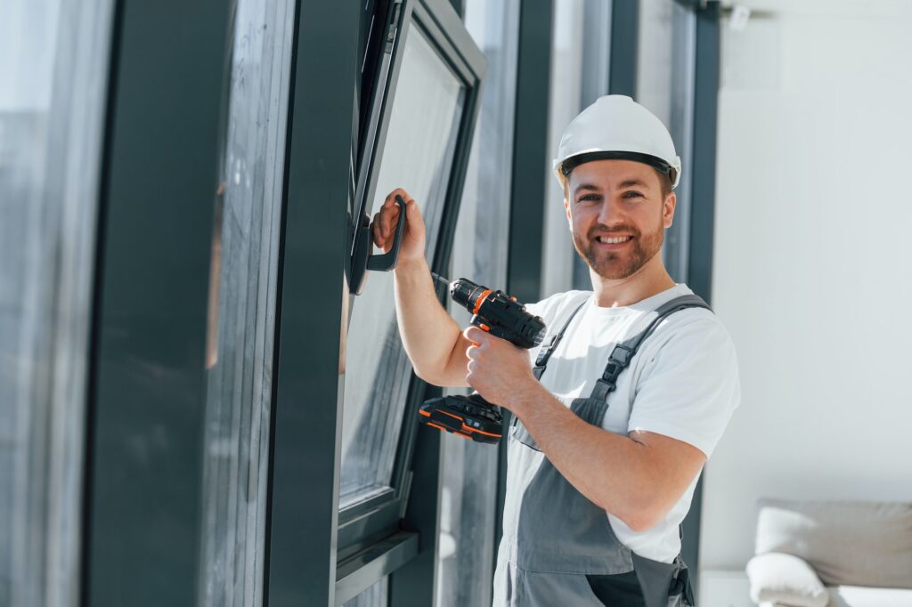 Using drill by installing windows. Repairman is working indoors in the modern room